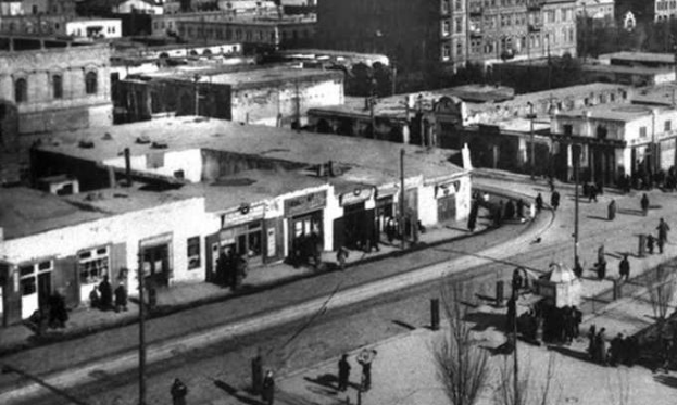 Schwarzes und weißes Foto einer Stadtstraße mit Fußgängern, Gebäuden, Bäumen, Strommasten und Drähten, die die historische städtische Umwelt widerspiegeln.
