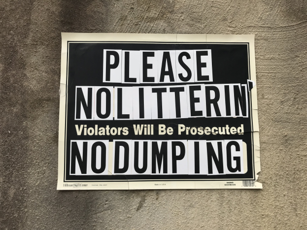Schwarz-weißes Schild an einem Gebäude mit der Aufschrift "Bitte keine Verschmutzung Verursacher werden strafrechtlich verfolgt Keine Ablagerung".