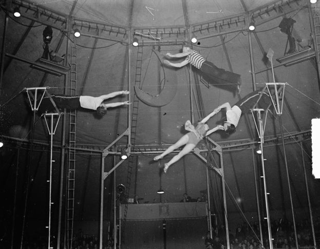 Schwarzes und weißes Foto von Akrobaten, die in einem Zirkuszelt performen, mit einer Zuschauermenge unten.