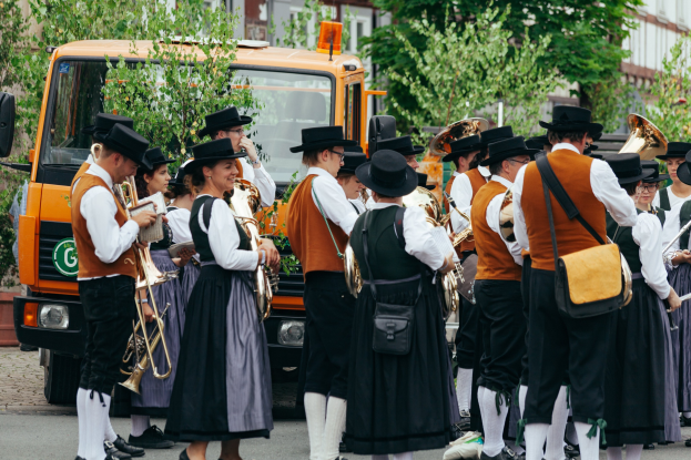 Gruppe von Menschen in traditioneller bayrischer Tracht, die auf der Straße spielen und Taschen tragen.