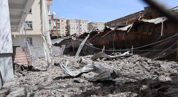 Die Auswirkungen eines israelischen Luftangriffs in Gaza-Stadt, der ein zerstörtes Gebäude mit Trümmern, eingestürzten Wänden, Metallstangen, einem Zaun, einer Treppe, nahen Gebäuden mit Fenstern, Bäumen und einem bewölkten Himmel zeigt.