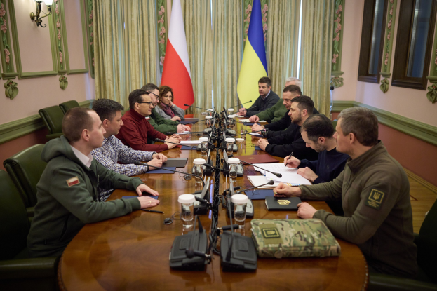 Eine Gruppe von Männern in einem formellen Setting, die um einen Holztisch mit Mikrofonen und Dokumenten sitzen und diskutieren.