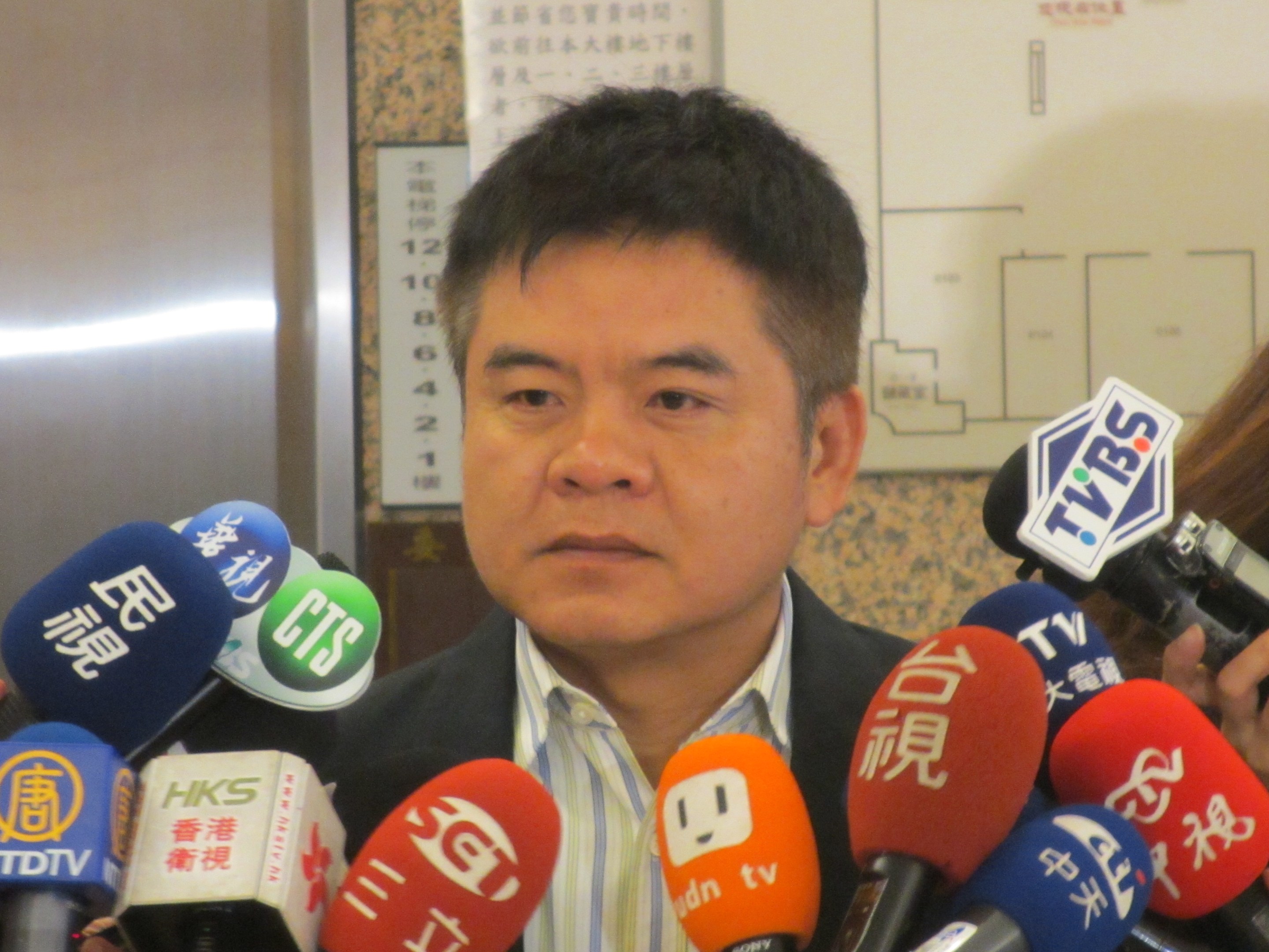 Ein Mann im Anzug spricht zu Reportern, während eine Frau eine Kamera hält.