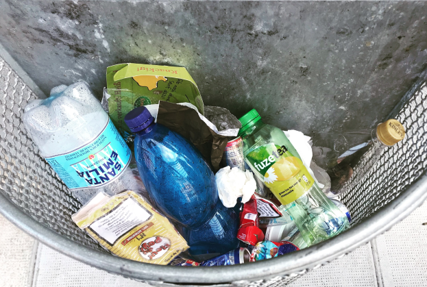 Ein Metallm├╝lltonne voller Plastikflaschen, T├╝ten und anderen Gegenst├Ąnden.