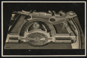 Schwarzes und weißes gerahmtes Foto eines detaillierten Modellkonzertsaals mit einer zentralen Kuppel, steinernen Wänden, Metalldach und einer hell erleuchteten Bühne, umgeben von einer Menge.