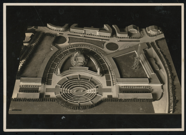 Schwarzes und weißes gerahmtes Foto eines detaillierten Modellkonzertsaals mit einer zentralen Kuppel, steinernen Wänden, Metalldach und einer hell erleuchteten Bühne, umgeben von einer Menge.