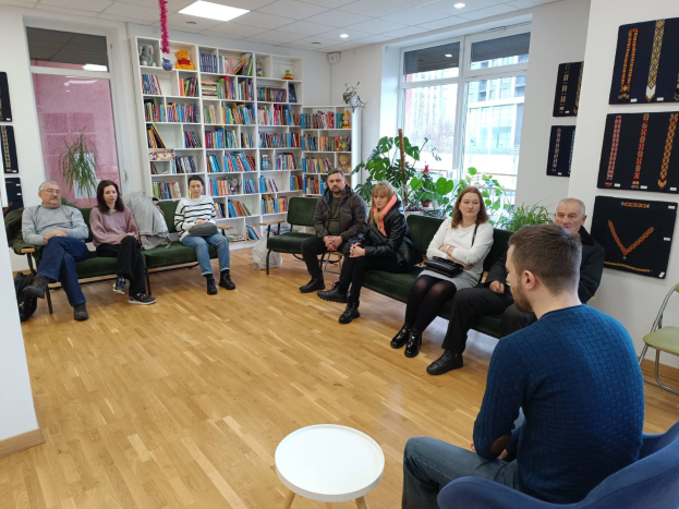 Eine Gruppe von Menschen sitzt um einen Tisch in einem Raum mit Bücherregalen, Pflanzen und einem Fenster und ist in ein Gespräch vertieft während eines Workshops über die Zukunft von Gesundheit und Wohlbefinden in Berlin, Deutschland.