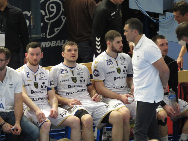 Eine Gruppe von Männern sitzt auf einer Bank, einige halten Flaschen, mit einem Banner im Hintergrund, auf dem "Nordkraque vs Bordeaux" steht.