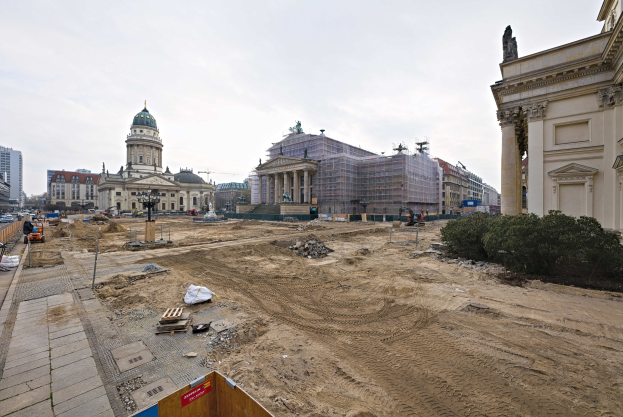 Eine Baustelle mit dem Berliner Dom als Hintergrund, Bäumen auf der rechten Seite und Fahrzeugen auf der linken Seite unter einem sichtbaren Himmel.