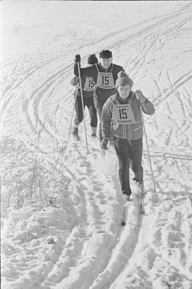 Drei Menschen mit Ski-Stöcken auf einem verschneiten Hügel Skilanglauf betreiben, in einem Schwarz-Weiß-Bild.