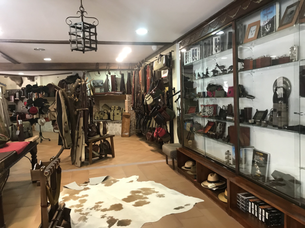 Ein vollgestelltes Boutique-Zimmer in Barcelona mit einem Kuhfellteppich, aufgehängten Kleidern, Hüten, Fotorahmen und verschiedenen Gegenständen in Schränken, beleuchtet von Deckenlampen und einem Kronleuchter.