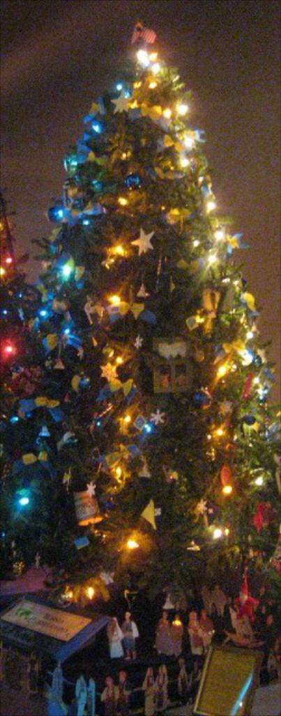 Ein geschmückter Weihnachtsbaum mit Menschenfiguren auf einem darunter stehenden Tisch.