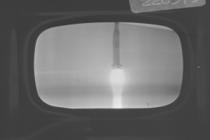 Schwarzes und weißes Foto eines Fernseherbildschirms mit einer Raketenstartszene und Text oben.