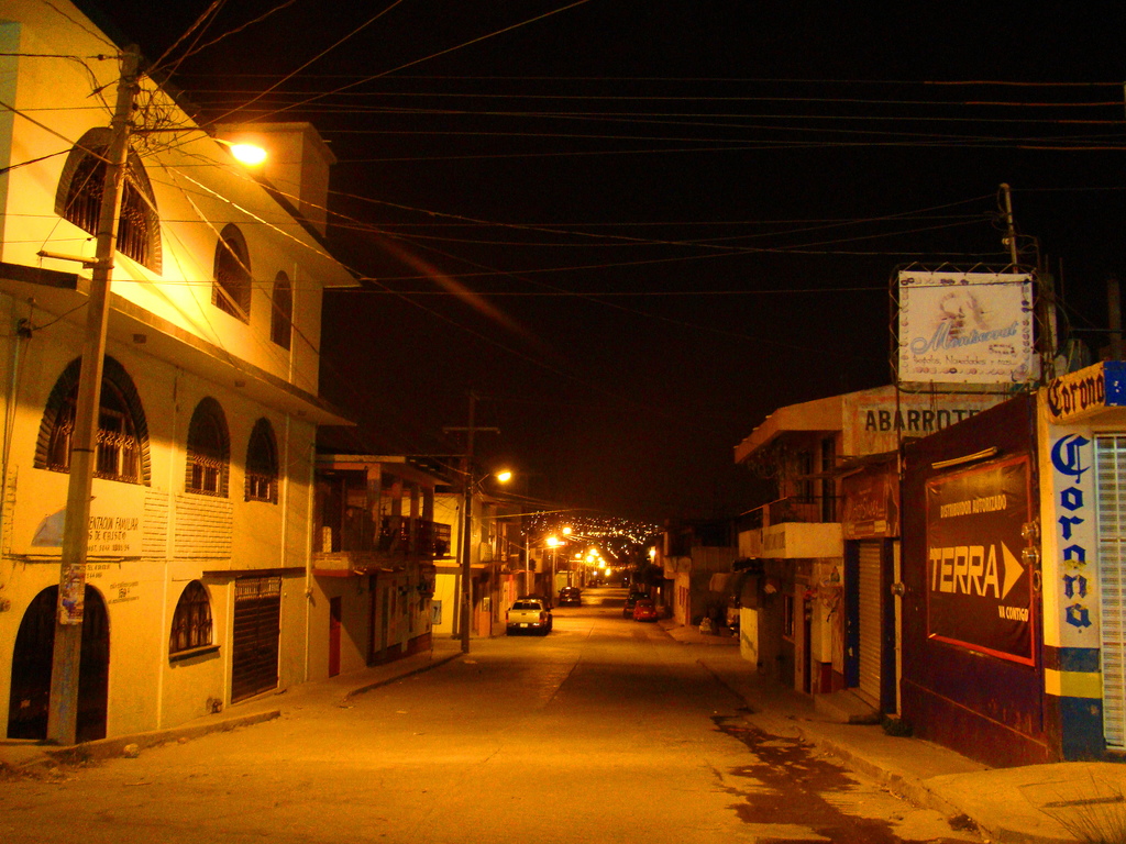 Eine Straßenszene mit Gebäuden und Strommasten auf beiden Seiten, ein paar geparkte Fahrzeuge vor den Gebäuden und eine Straße in der Mitte.
