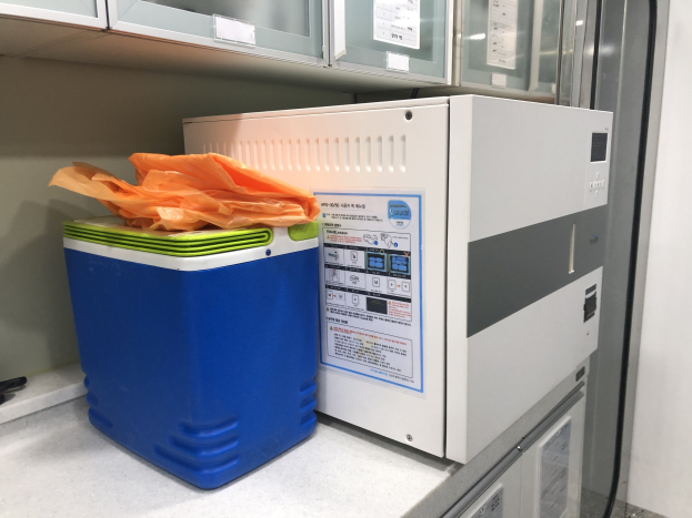 Blauer und weißer Kühler auf einer Arbeitsplatte neben einer Ultraschall-Reinigungsmaschine mit einer Plastikabdeckung oben drauf, andere Gegenstände auf der Arbeitsplatte und Schränke darüber.
