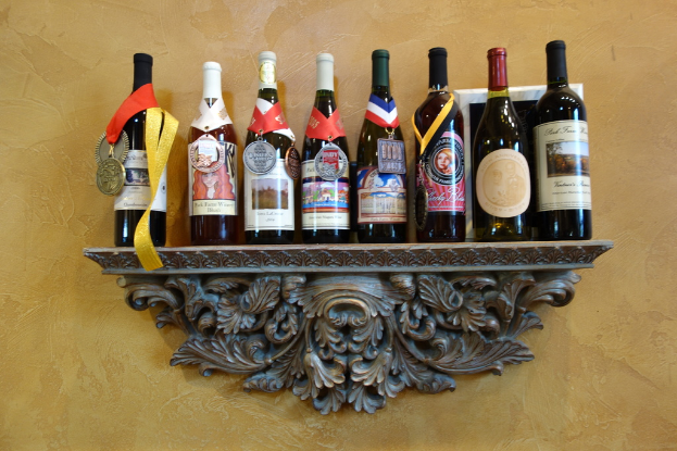 Mehrere Weinflaschen auf einem Regal, eine mit einer sichtbaren Medaille, vor einer hellgelben Wand.
