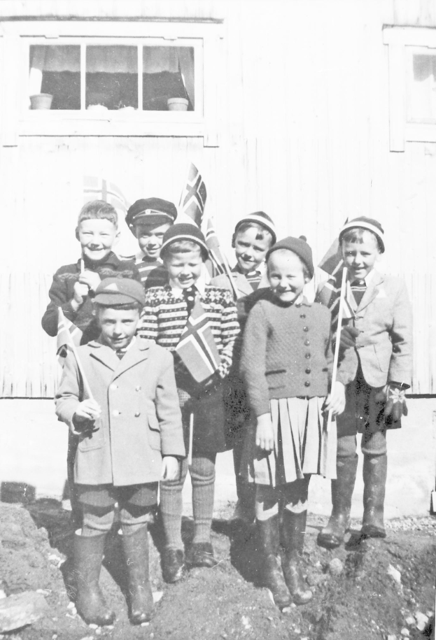 Eine Gruppe strahlender Kinder steht nebeneinander vor einem Gebäude, jeder hält eine Fahne, auf einem Schwarz-Weiß-Foto einer schwedischen Schule mit einer Wand und einem Fenster im Hintergrund.
