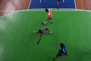 Eine Gruppe von Männern, die Fußball auf einem Platz spielen, einer hält den Ball, während die anderen um ihn herum laufen, alle tragen Schuhe.