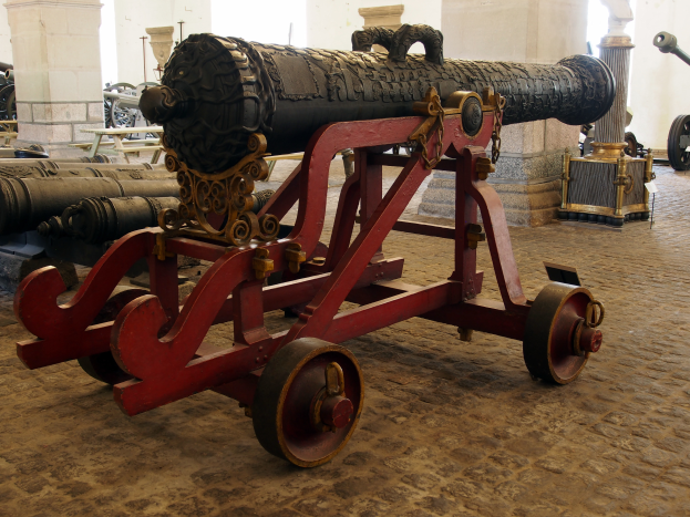 Eine alte Kanone in einem Museum ausgestellt, umgeben von anderen Kanonen und Pfeilern im Hintergrund.
