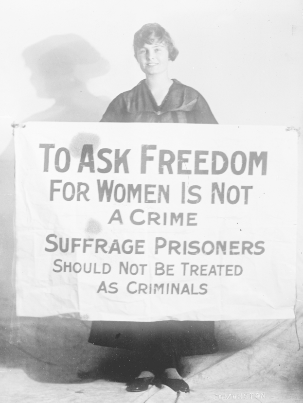 Schwarz-weiß-Foto einer Frau, die ein Banner hält, auf dem steht: "Für die Freiheit der Frauen zu kämpfen ist kein Verbrechen, Suffragetten sollten nicht wie Kriminelle behandelt werden."