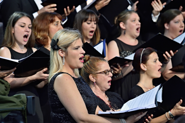 Eine Gruppe von Frauen, die in einem Chor singen, einige halten Bücher, mit einer Person, die im Vordergrund sitzt und einem unscharfen Hintergrund.