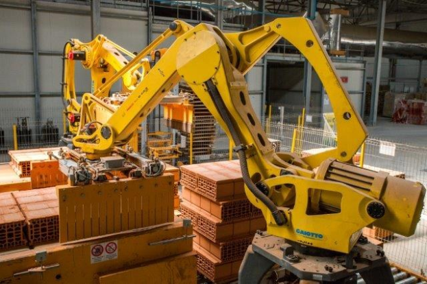 Großes Industriegebäude mit gestapelten Kisten, Überkopfkranen, Zaun, Pfählen und einer fernen Wand in einer automatisierten Fertigungsumgebung.