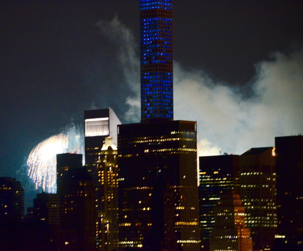 Gebäude mit Lichtern, Feuerwerk und Rauch im Hintergrund unter einem Himmel.