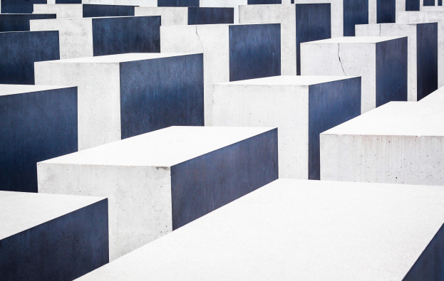 Eine große Anzahl rechteckiger Betonplatten in verschiedenen Höhen, die in einem Gittermuster auf einem geneigten Feld angeordnet sind, mit einer ernsten Atmosphäre, die das Holocaust-Mahnmal für die ermordeten Juden Europas in Berlin, Deutschland, darstellt.