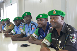Eine Gruppe von Polizeibeamten sitzt an einem Tisch während einer Schulung, mit Mobiltelefonen und anderen Gegenständen auf dem Tisch, in einem Raum mit Fenstern und Deckenleuchten.