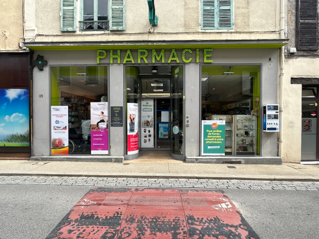 Eine Apotheke mit Glasw├Ąnden und -t├╝ren an einer Stra├čenecke, mit Plakaten an den W├Ąnden und einer Stra├če unten.
