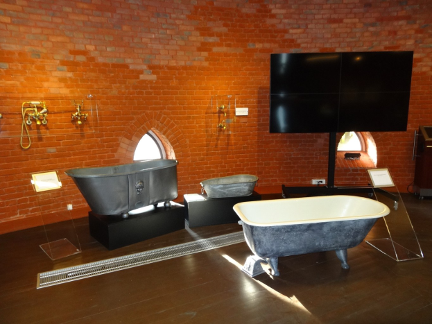 Ein gemütliches Badezimmer mit einer Backsteinwand, einer zentralen Wanne, an der Wand montierten Hähnen auf der linken Seite und einem an der Wand montierten Fernseher auf der rechten Seite.