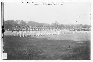 Gruppe von Menschen auf dem Boden stehend, einige mit Gewehren, Bäume und Hügel im Hintergrund, unter einem bewölkten Himmel, mit "cadets on parade west point"-Text oben.