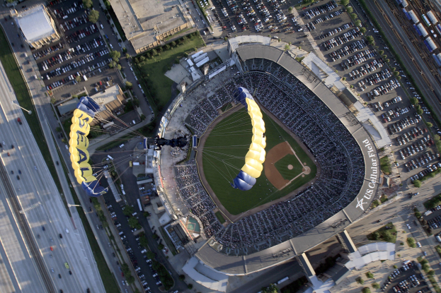 Luftaufnahme eines Baseball-Stadions mit zwei Paragleitern darüber, umgeben von Gebäuden, Bäumen, Straßen, Fahrzeugen und Gras.
