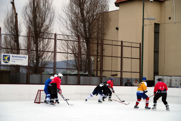 Menschen, die Eis hockey auf einem Eis spielen mit Gebäuden, Bäumen und einer Straßenlaterne im Hintergrund.
