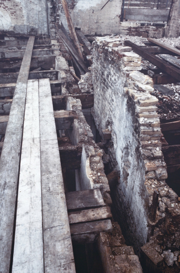 Altbau im Abriss, mit verstreuten Holzplanken und Steinen im Vordergrund und einer remaining Wand im Hintergrund.