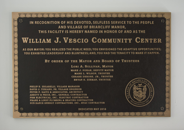Plaque auf einer Gebäudewand mit der Aufschrift "William J. Vesco Community Center" in weißer, fetter, zentrierter Schrift auf einem schwarzen rechteckigen Hintergrund.