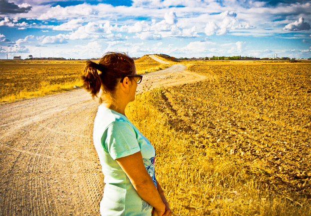 Eine Frau steht auf einem schlammigen Weg, der von Landwirtschaftsland und Bäumen gesäumt ist.