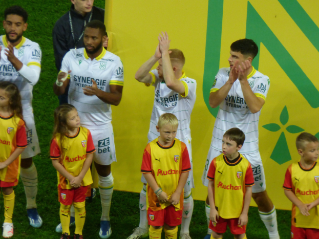 Eine Gruppe junger Menschen in Fußballtrikots steht auf einem Fußballfeld und klatscht feiernd mit einer «Ligue 1»-Tafel im Hintergrund.