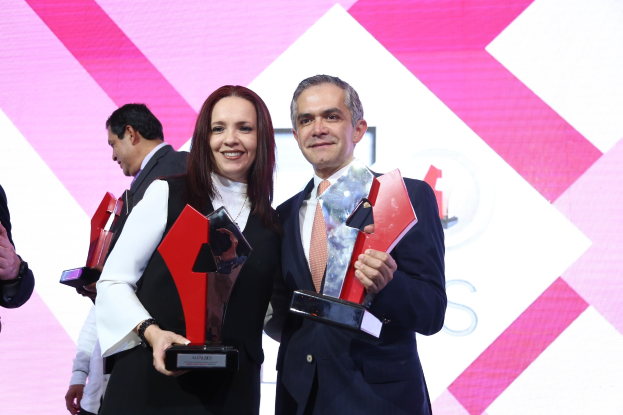 Zwei strahlende Menschen mit Auszeichnungen auf einer Bühne, im Hintergrund ist ein Bildschirm zu sehen.