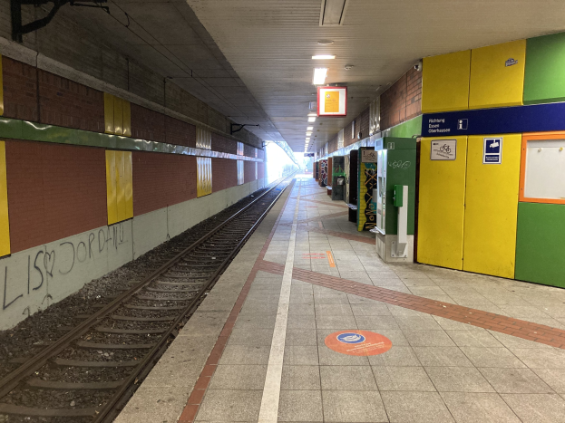 Ein Bahnsteig in Berlin Hauptbahnhof, Deutschland, mit einem Zug auf den Schienen, Deckenleuchten, Graffiti an einer linken Wand und ein paar Gegenständen auf der rechten Seite.