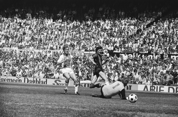 Schwarzes Foto von Fussballspielern im Einsatz auf einem Feld mit Zuschauern im Hintergrund und einem Bundesliga 1978-79 Ajax 1-1 Hannover 96-Banner.