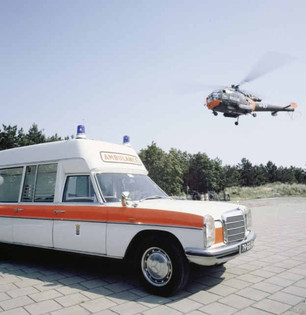 Ambulanz vor Hubschrauber mit Bäumen und einem klaren blauen Himmel im Hintergrund geparkt.
