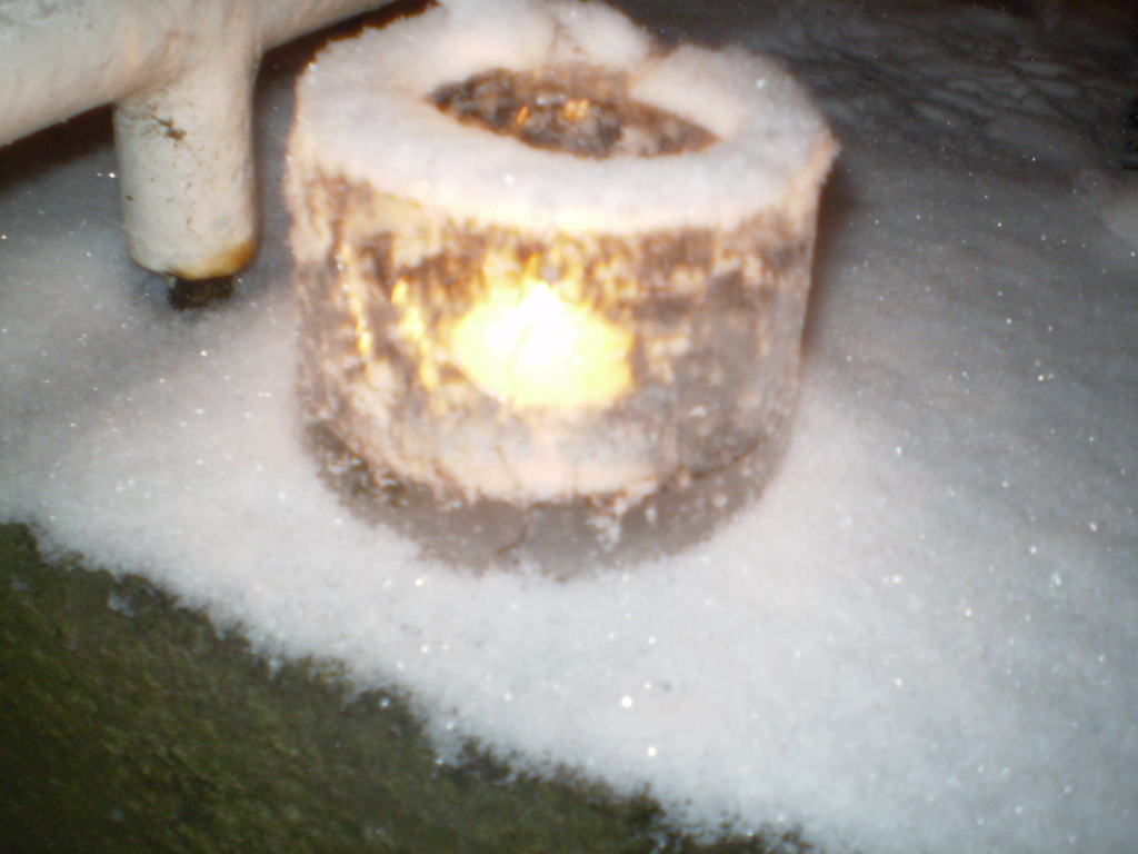 Eine Kerzenflamme mit Schnee im Hintergrund und eine mögliche Pfeife im oberen linken Eck.
