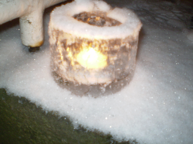 Eine Kerzenflamme mit Schnee im Hintergrund und eine mögliche Pfeife im oberen linken Eck.