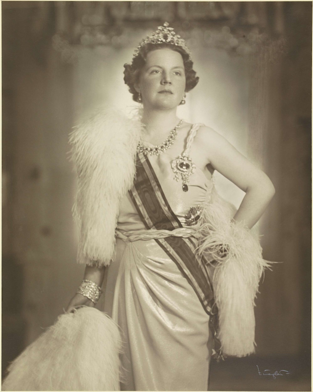 Schwarz-weiß-Foto von Queen Elizabeth II in einem Kleid und einer Krone mit unscharfem Hintergrund und Text unten.