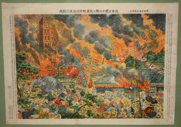 Ein Plakat an einer Gebäudewand mit einer Darstellung einer chaotischen Feuerszene mit Menschen, Tieren, Wagen, Fahnen, Bäumen, Gebäuden und anderen Gegenständen, die in Flammen stehen, mit sichtbarem Text auf dem Plakat.