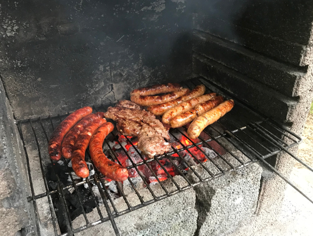Grill mit Würstchen und Fleisch über Kohle und Feuer im Freien auf Gras.
