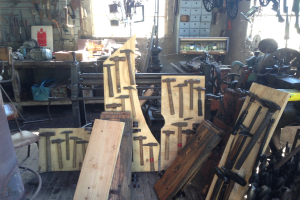 Ein mit Werkzeugen, Geräten und Holzplanken gefüllter Werkraum, der einen Stuhl links, Werkzeuge an der Wand und ein Fenster im Hintergrund zeigt.