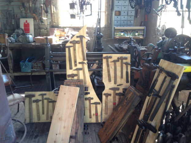 Ein mit Werkzeugen, Geräten und Holzplanken gefüllter Werkraum, der einen Stuhl links, Werkzeuge an der Wand und ein Fenster im Hintergrund zeigt.