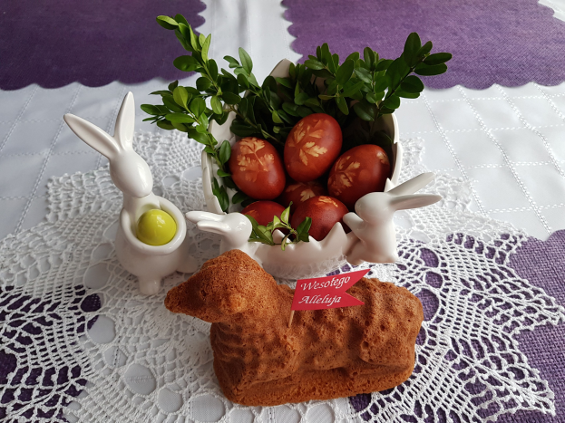 Ein Tisch mit einer Decke darauf hält eine Schüssel voller bunter Ostereier mit Osterhasen-Figuren darauf.
